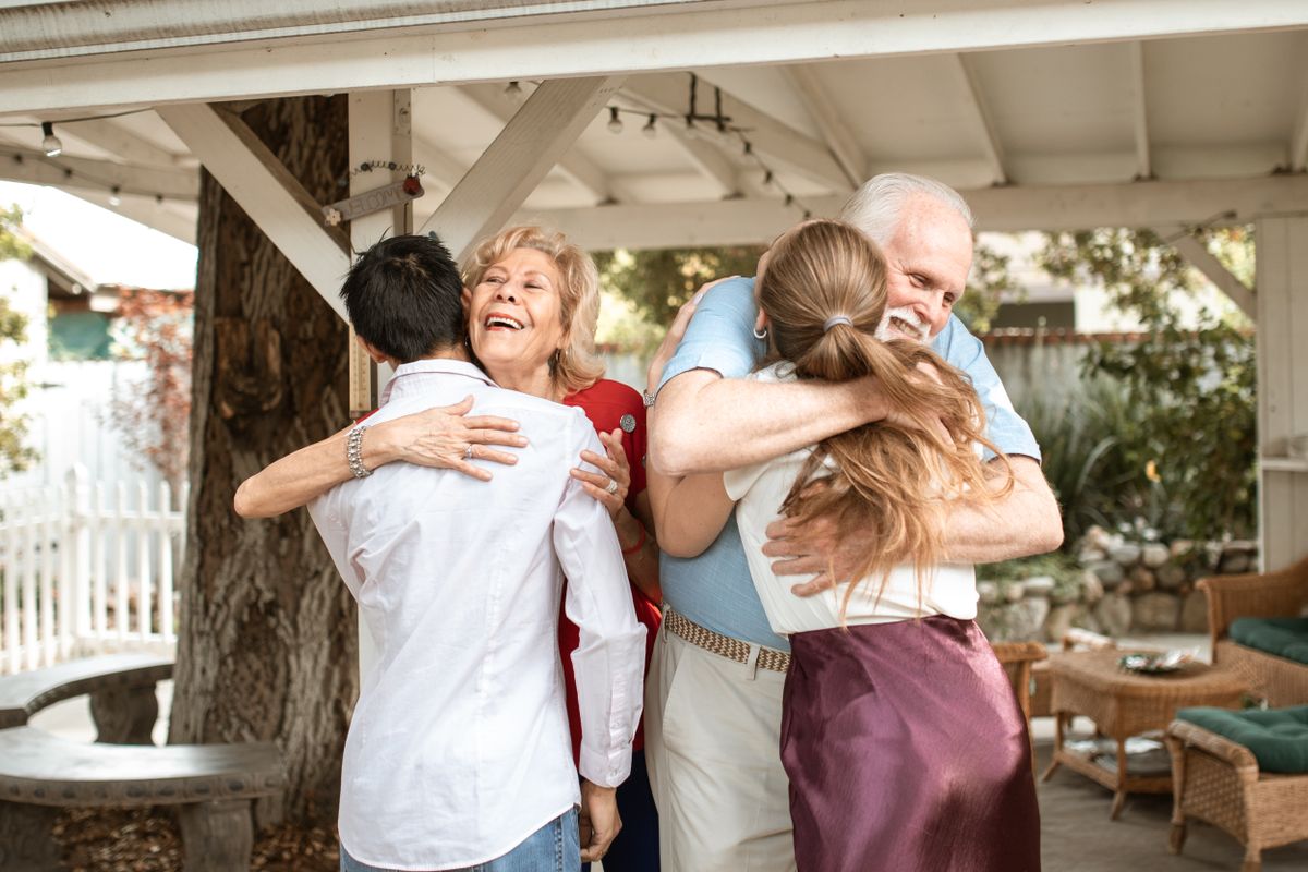 An older couple hugging their adult children under a covered backyard patio at a family gathering